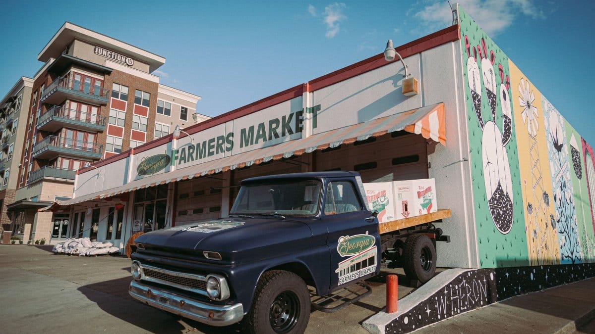 A classic truck parked outside a colorful farmers market in Plano, Texas, under a clear sky.