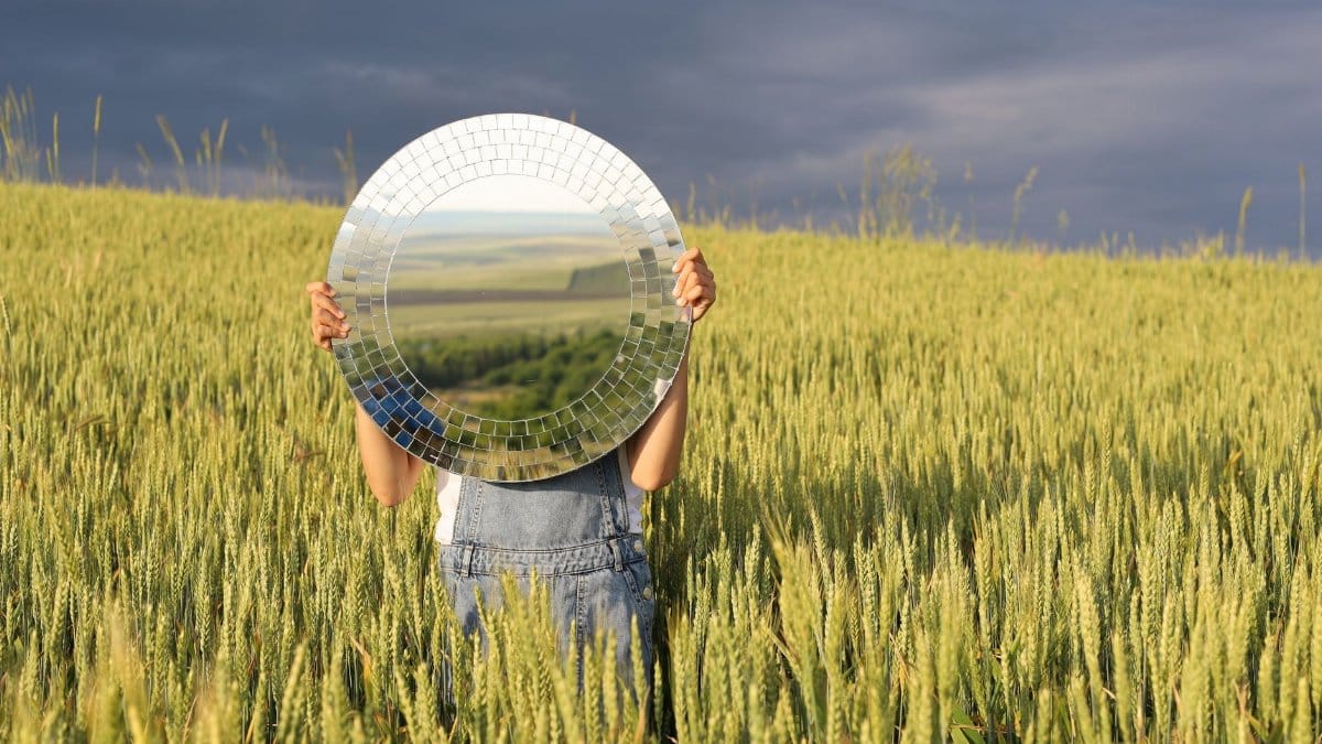 Person holding a mirror in a lush wheat field creates a unique visual illusion.