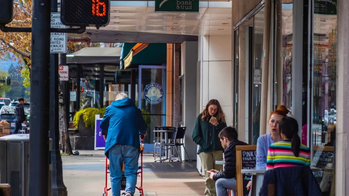 Bustling city street with people walking and sitting at a sidewalk café during the day.