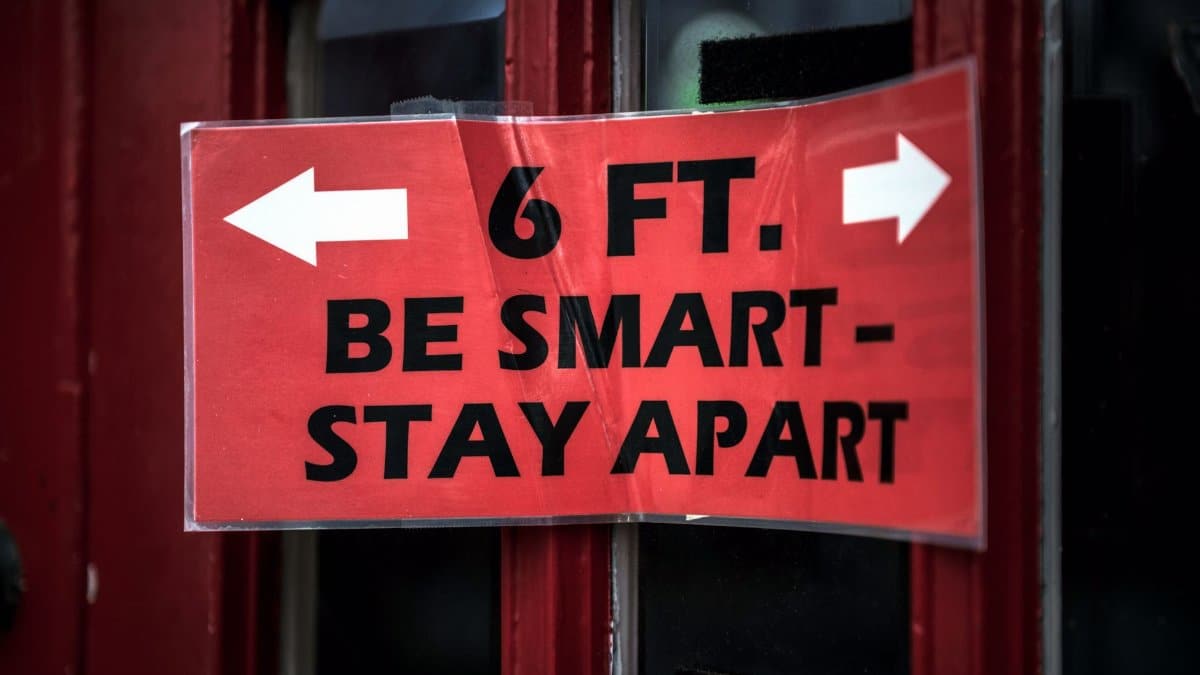 Red sign with distancing message: '6 ft. Be Smart - Stay Apart' on a door.