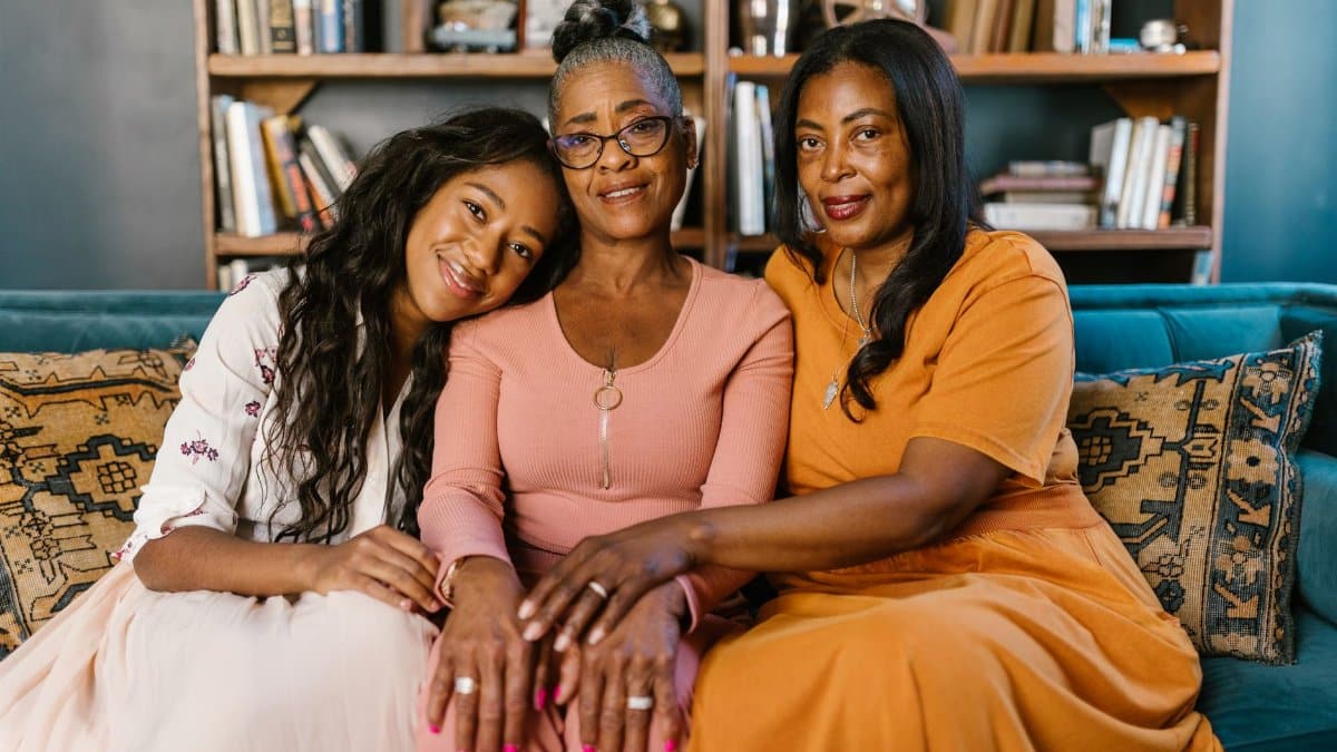 Three beautiful black women sitting together on a couch, smiling indoors.