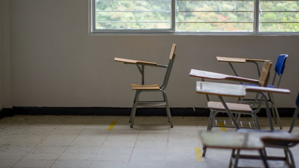 Quiet empty classroom interior with school desks by a large window.