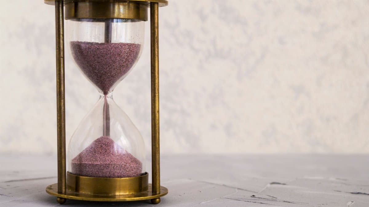 A traditional hourglass with pink sand, symbolizing time and patience on a textured surface.