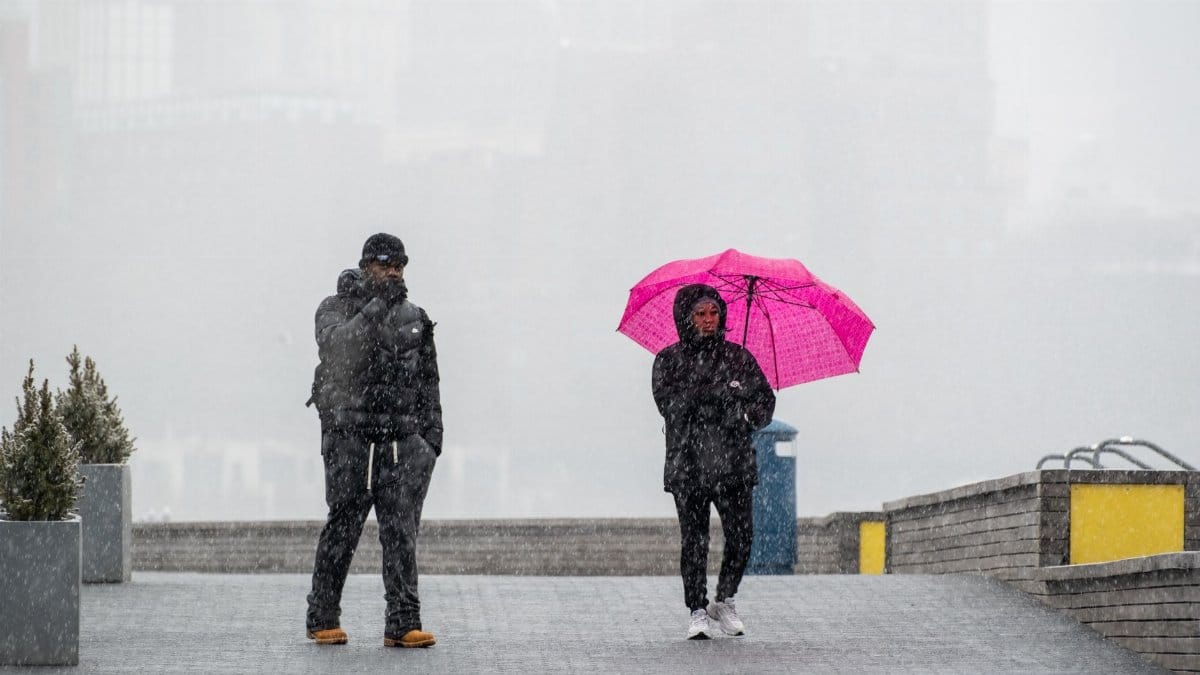Two people walking in snowy urban setting, one with a pink umbrella, capturing city life in winter.