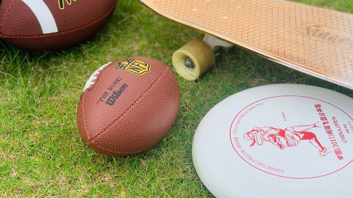 A close-up of sports equipment including a football, skateboard, and frisbee on grass.