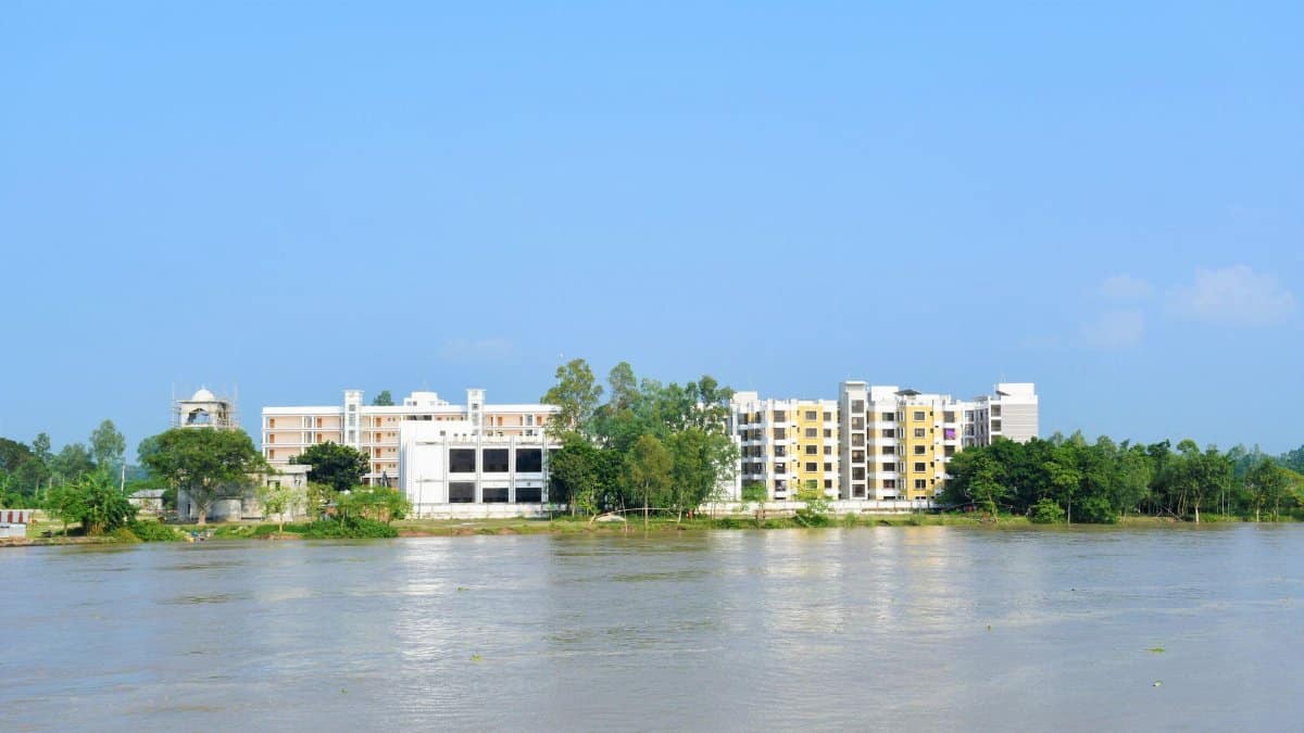 A serene view of buildings by the river in Pirganj, Bangladesh, under clear blue skies.