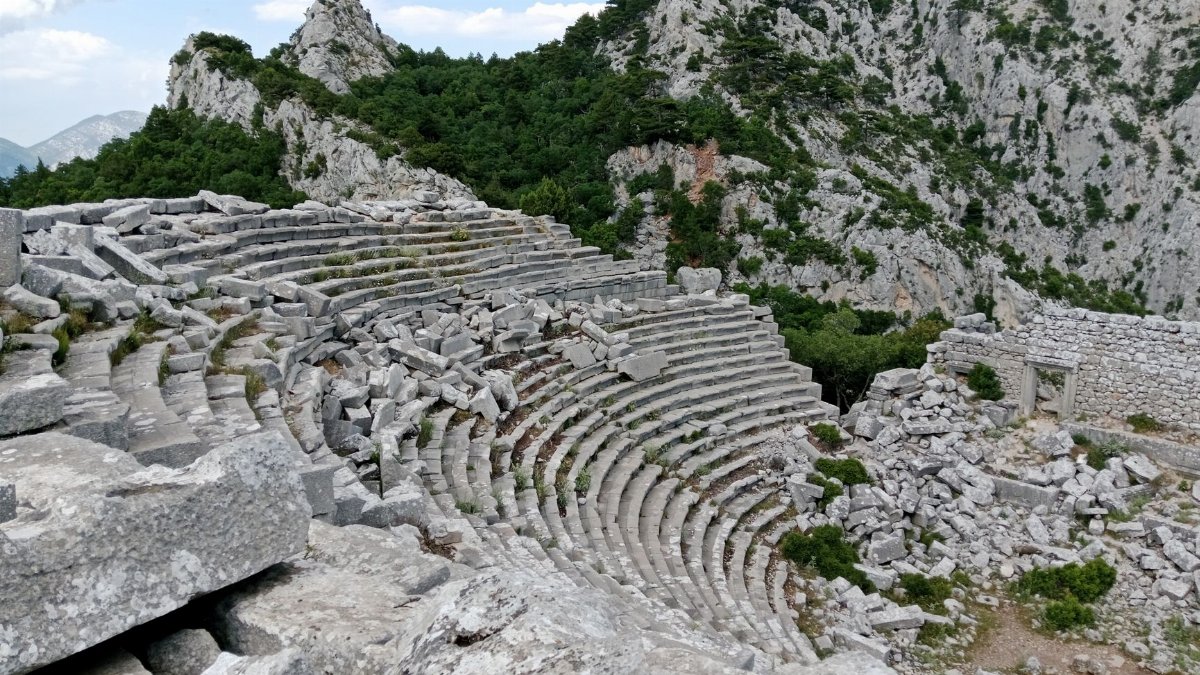 Ruins of an ancient amphitheater nestled within a rocky mountain landscape.