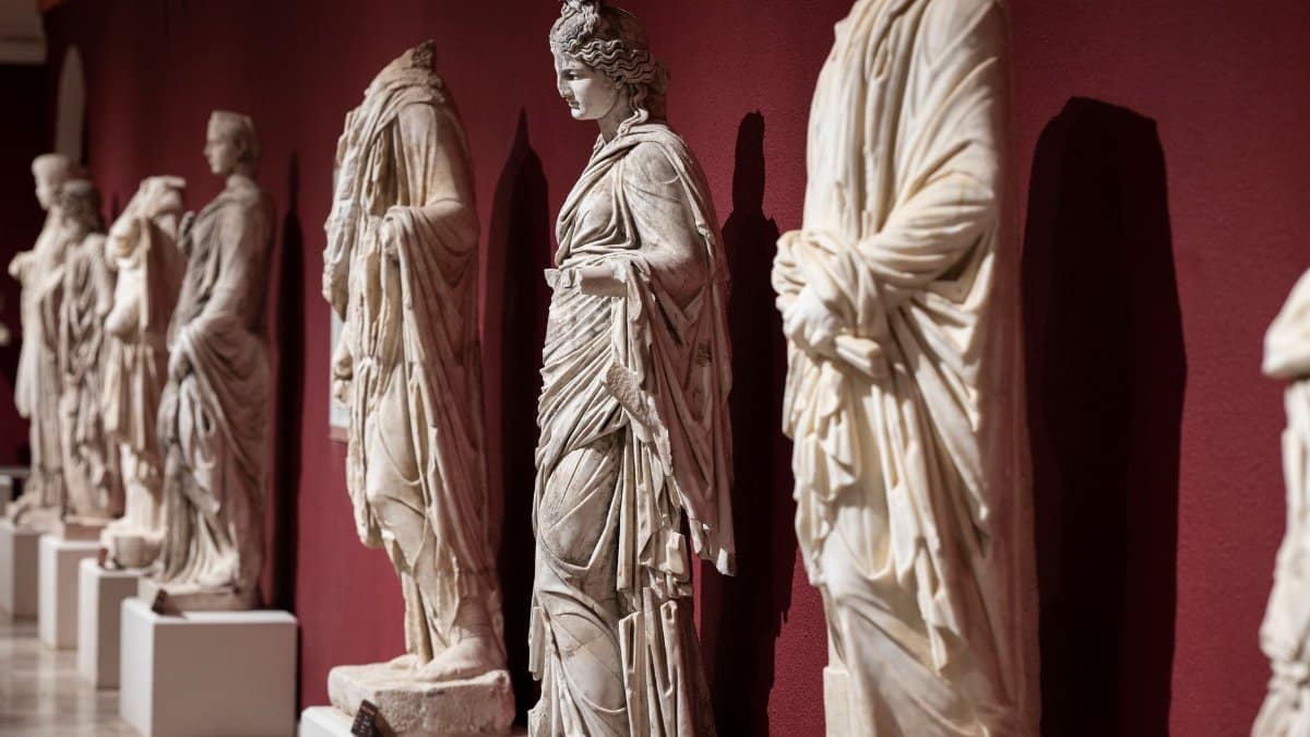 Collection of ancient Roman statues on display in a museum with a red wall backdrop.