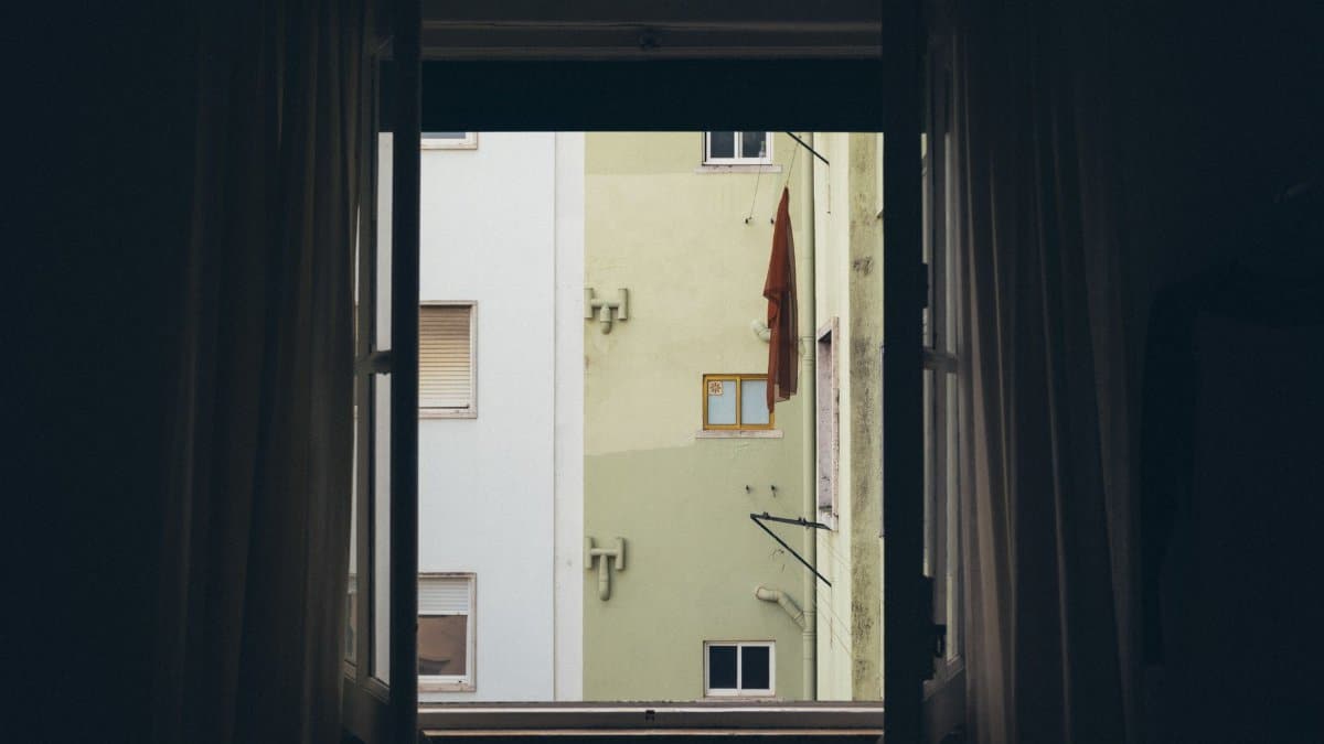 A view of an urban apartment building facade framed by an open window.