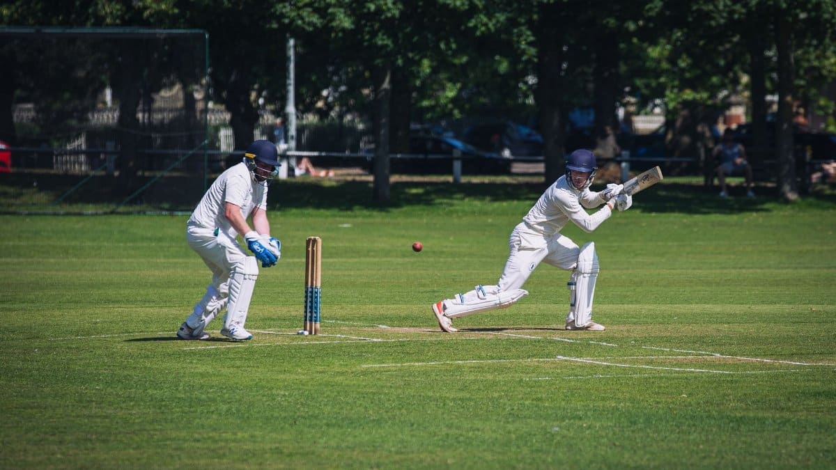 Two cricket players in action during a sunny match on a lush green field in London.