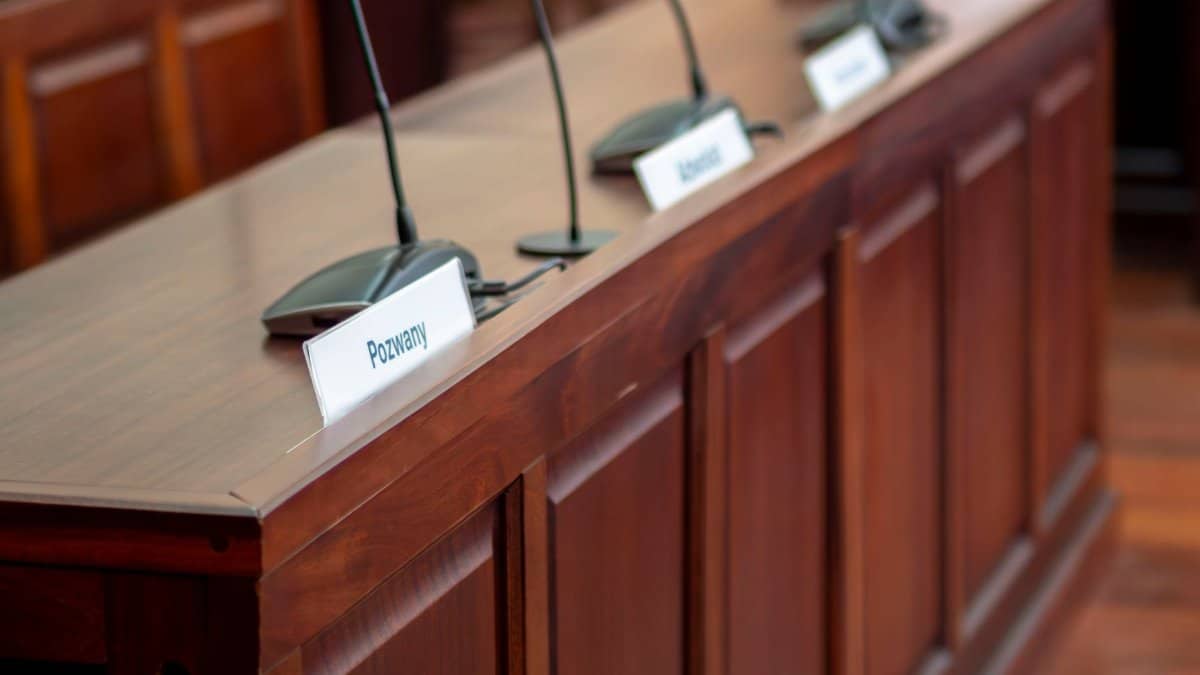 Empty courtroom desk with microphones and nameplates in a Polish court setting.