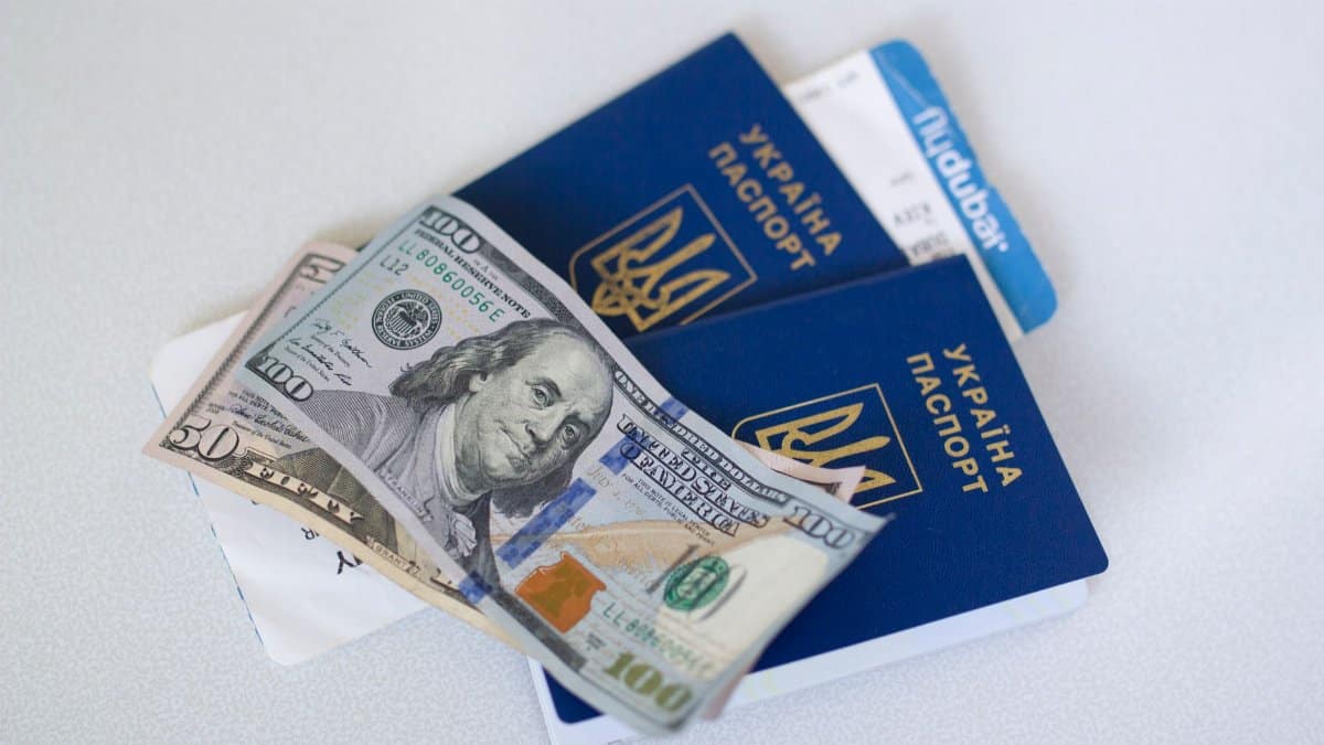 Close-up view of Ukrainian passports with US dollar bills, symbolizing travel readiness.