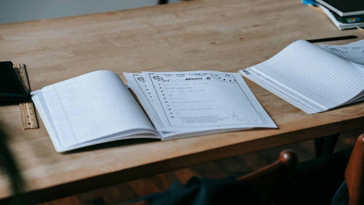 Stationery and opened copybooks with empty sheets placed on wooden desk in light contemporary school