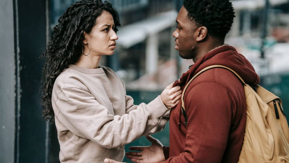 Side view of young unhappy diverse couple in casual clothes standing together and looking at each other