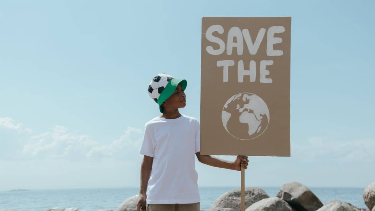 Young boy at beach holding a sign promoting environmental awareness and earth conservation.