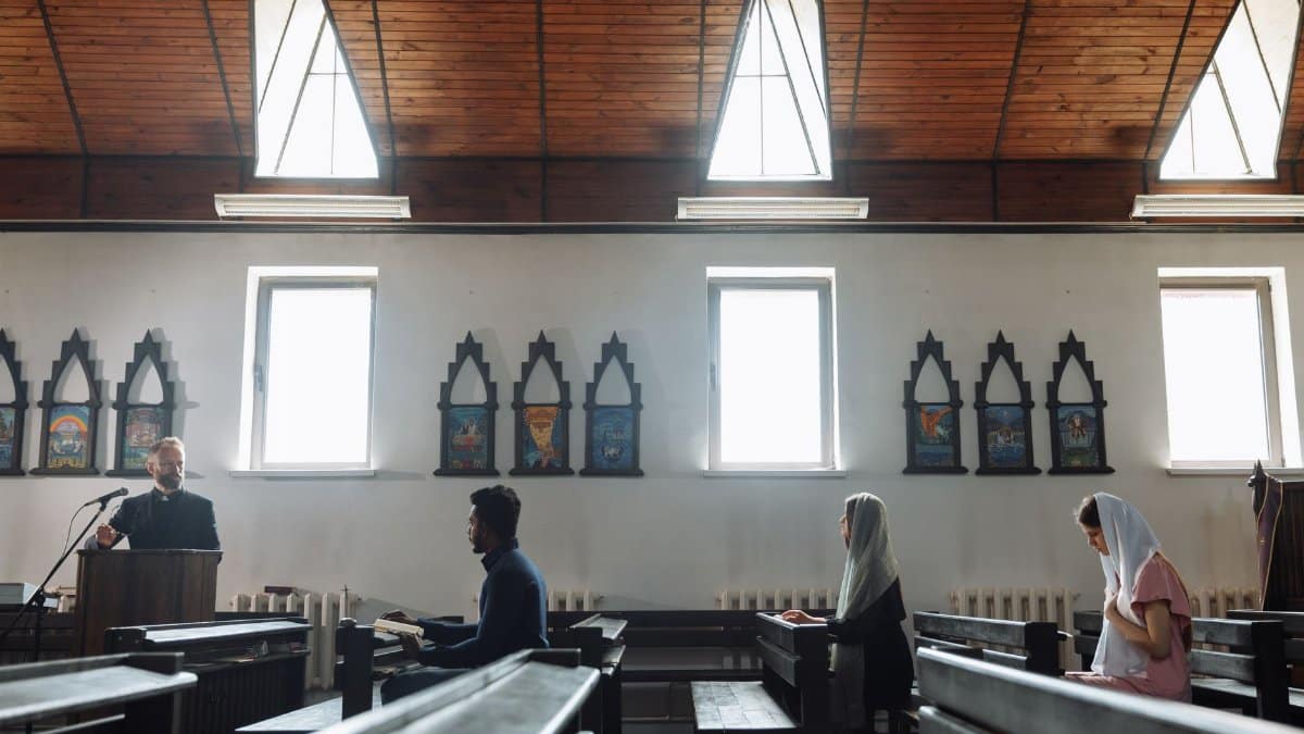 A serene church interior with people praying and a priest presiding from a pulpit.