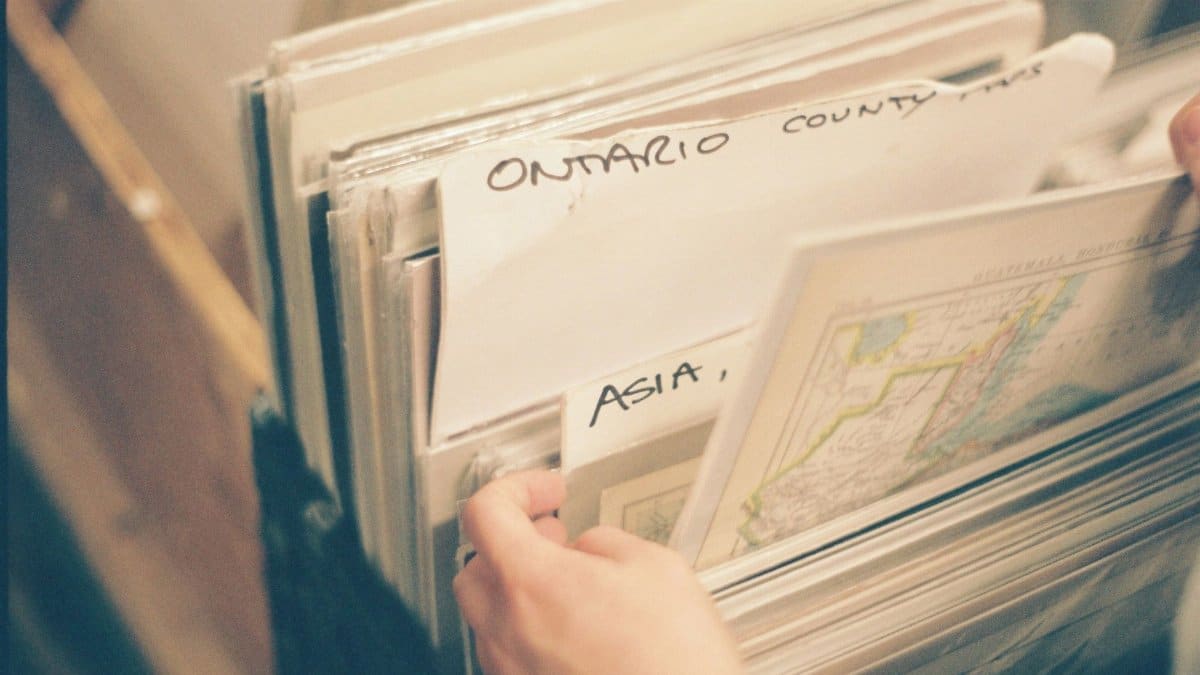 From above of anonymous person selecting paper maps with captions in stack while spending time in library with blurred background
