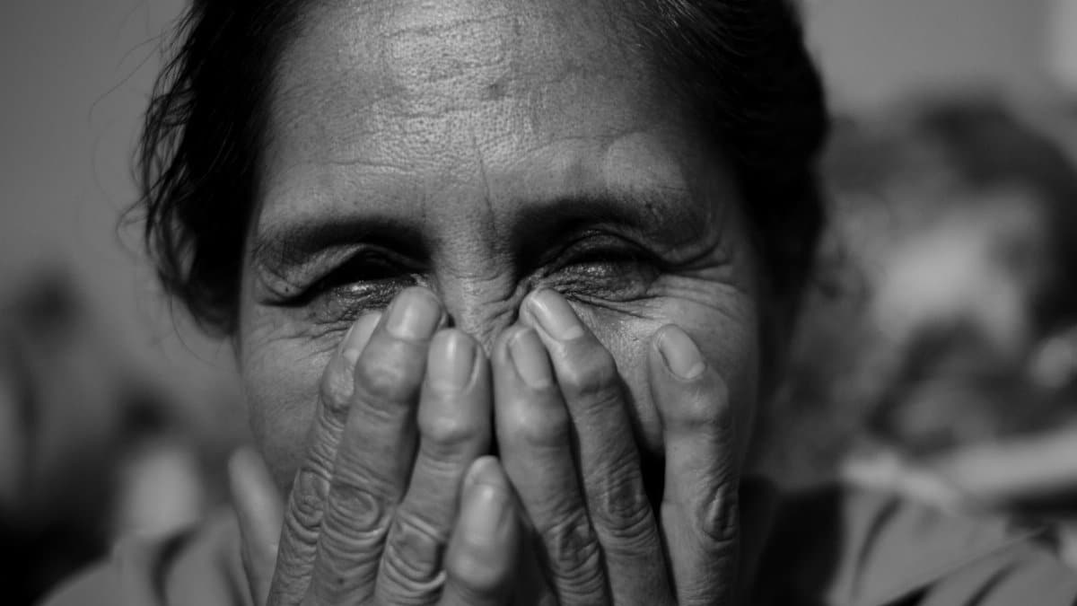 Black and white portrait of an elderly woman smiling with her hands over her face.