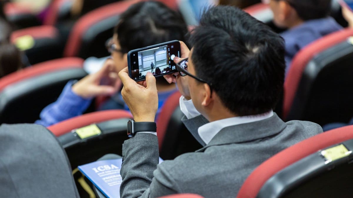 Businessman photographs presentation screen on smartphone at a conference.