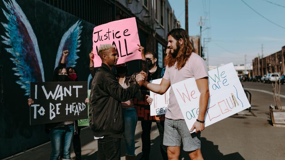 A diverse group of people at an outdoor protest rally holding signs promoting justice and equality.