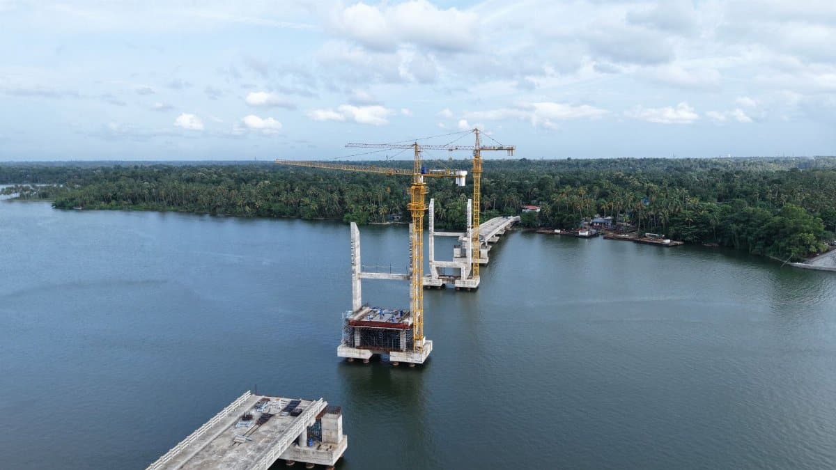 Aerial shot of a bridge under construction over a river in Kerala, India with cranes and lush greenery.