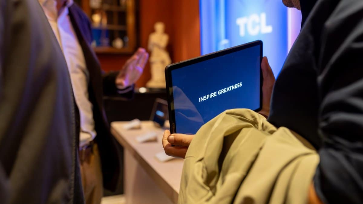 A man holding a tablet with 'Inspire Greatness' displayed at a tech event indoors.