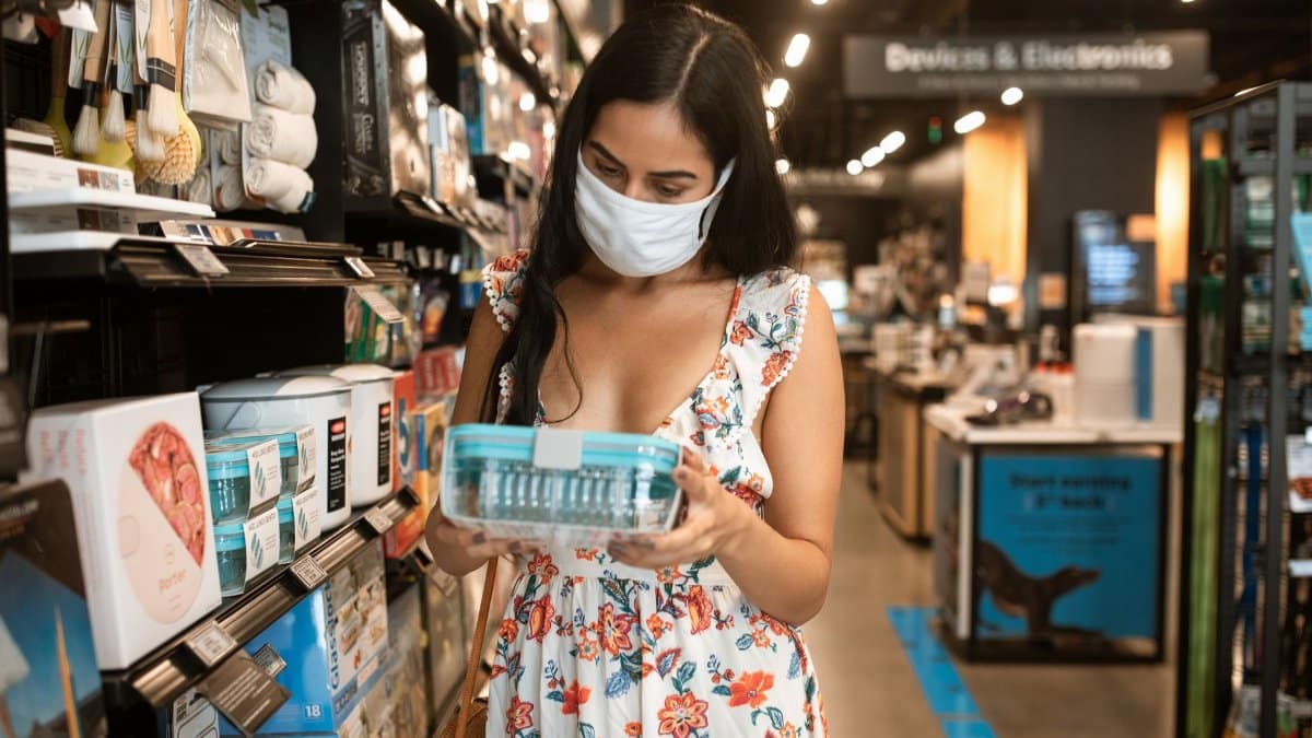 Young woman in floral dress shopping with a face mask in a store aisle.
