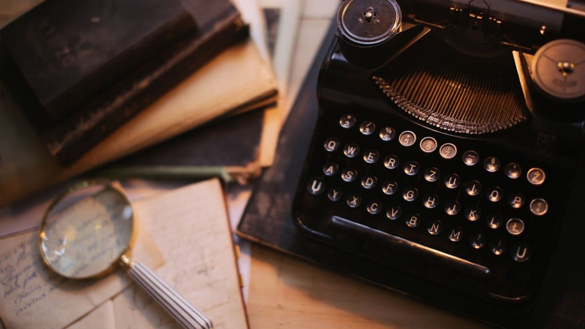 A vintage typewriter with a magnifying glass and old books on a desk, evoking nostalgia.