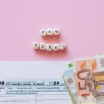 Top view of tax form, euro banknotes, and 'Pay Taxes' letter blocks on pink background.