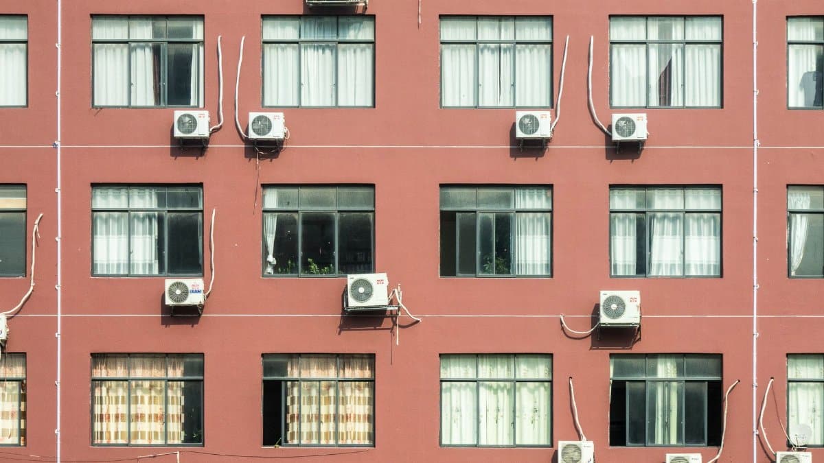 Red building exterior with multiple windows and air conditioners, showcasing urban architecture.