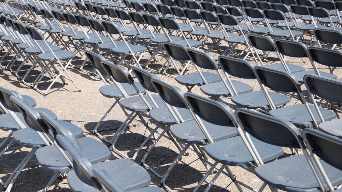 An array of empty folding chairs arranged outdoors, casting shadows in bright sunlight.