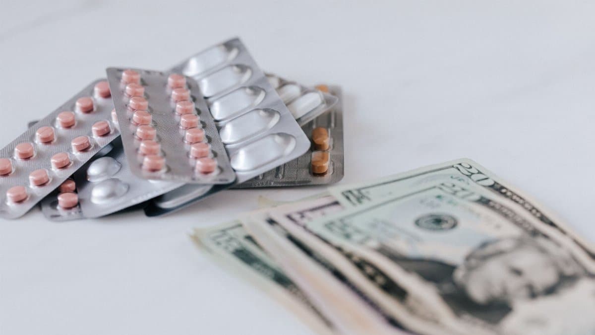 Multicolored pills in silver blisters on white surface near heap of paper money representing expensive pharmacy