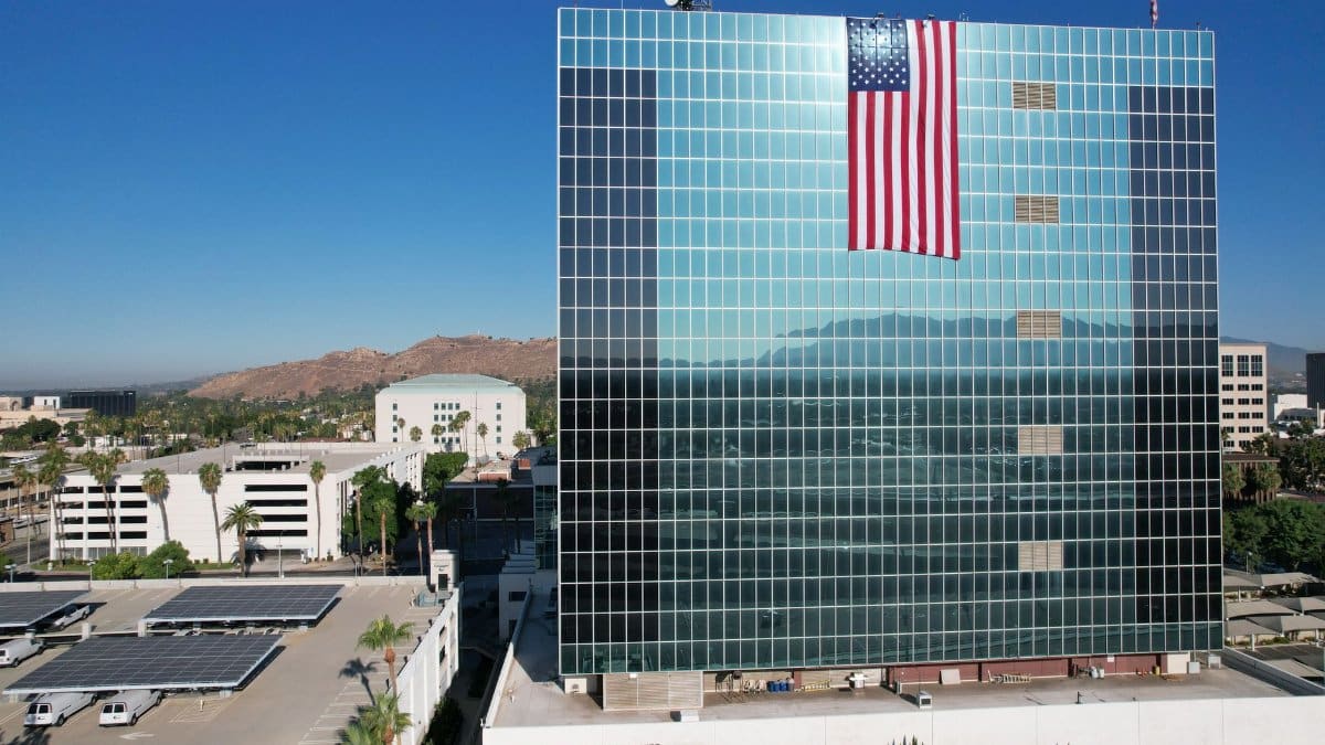 Huge American flag on glass facade building in Riverside, CA, under clear blue sky.