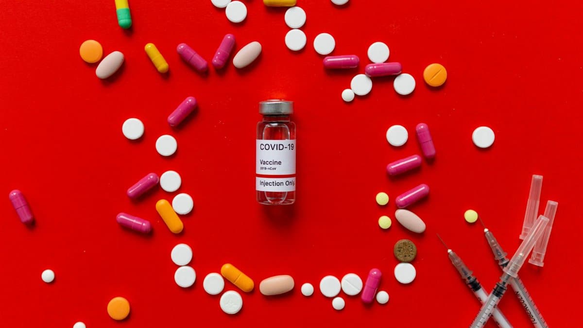 Colorful tablets and COVID-19 vaccine vial on a red background with syringes, symbolizing healthcare.