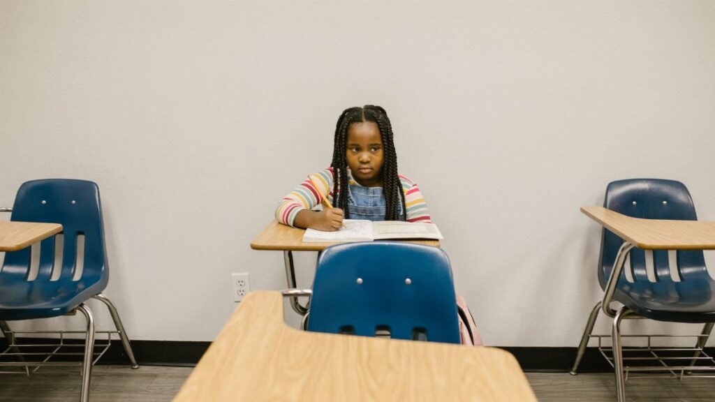 A young girl sits alone in a school classroom, symbolizing the impact of bullying.