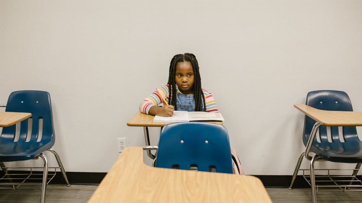 A young girl sits alone in a school classroom, symbolizing the impact of bullying.