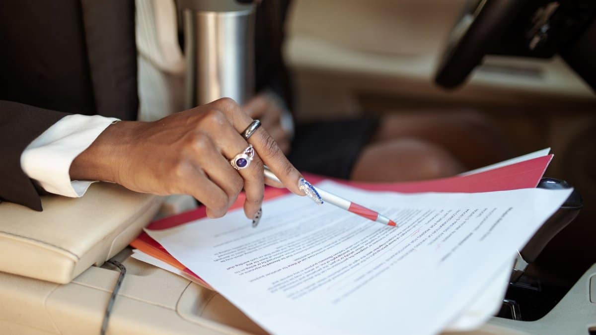 A professional reviewing documents in a car interior, focusing on hand and paperwork.