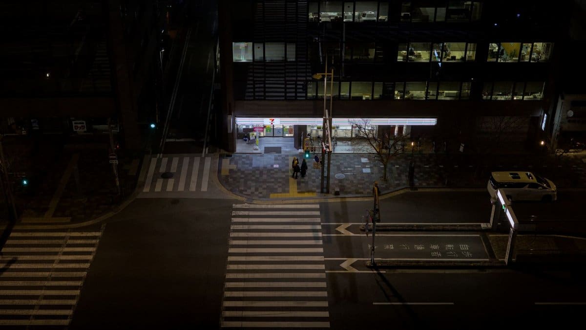 Aerial view of a quiet street in Kyoto at night, featuring a zebra crossing and a convenience store.