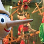 Wooden Pinocchio figure with puppets in a shop window display creates a whimsical scene.