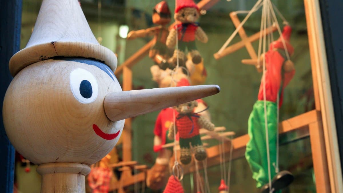 Wooden Pinocchio figure with puppets in a shop window display creates a whimsical scene.