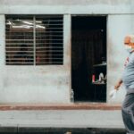 Senior man wearing mask walking past a weathered building in Havana, Cuba, during daytime.