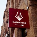 A red sign featuring a cannabis emblem on a city building facade, indicating a store direction.