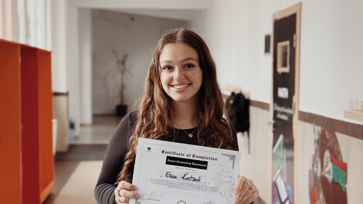 Smiling woman proudly displays certificate in a school corridor. Achievement and success captured.