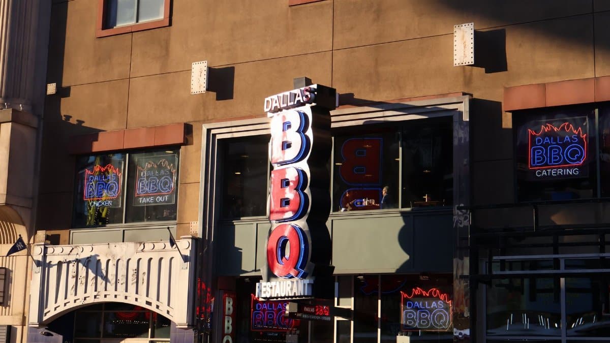 Neon signage of Dallas BBQ Restaurant illuminated in an urban environment at sunset.