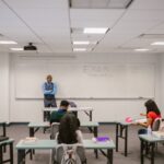 A classroom setting with a teacher proctoring an exam, students focused on their tests.