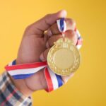 Close-up of a hand holding a gold medal with a colorful ribbon, symbolizing victory and achievement.