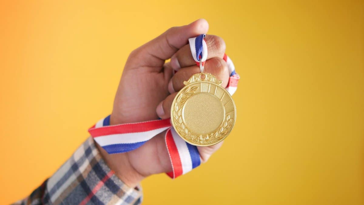 Close-up of a hand holding a gold medal with a colorful ribbon, symbolizing victory and achievement.