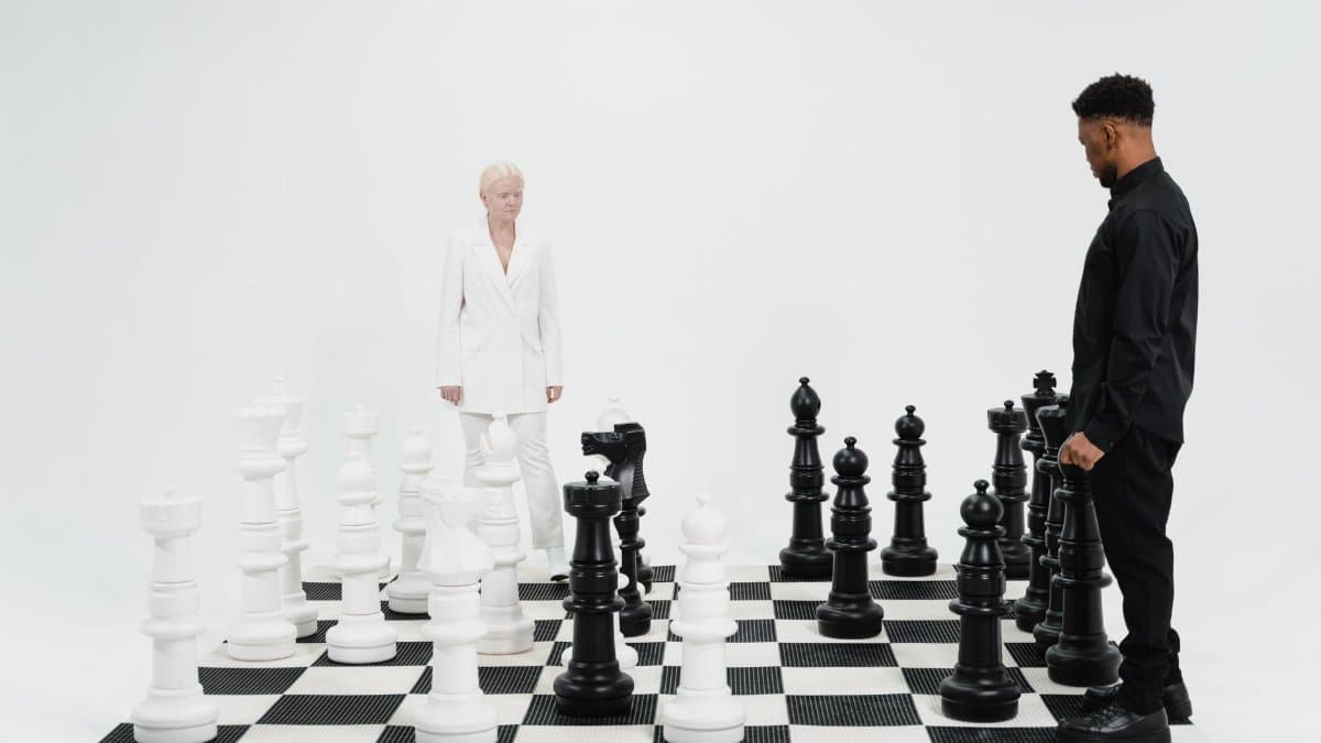 Two people engaged in a strategic chess game with oversized black and white pieces.