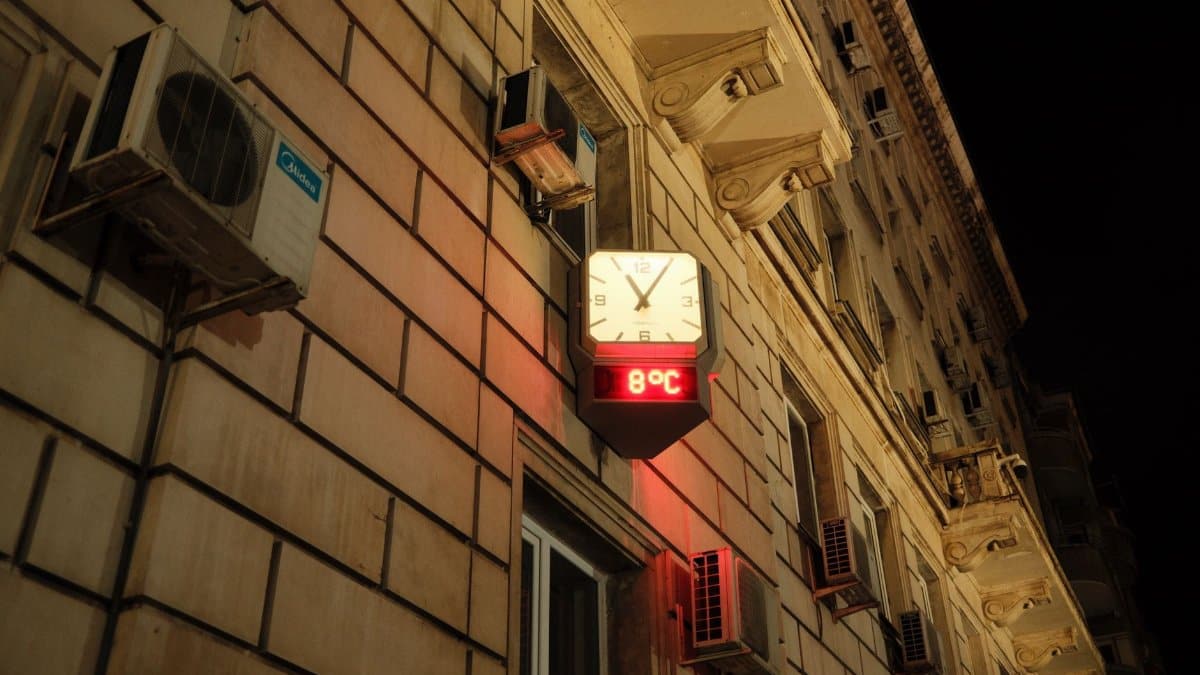 Illuminated wall clock showing time and temperature on a building facade at night.