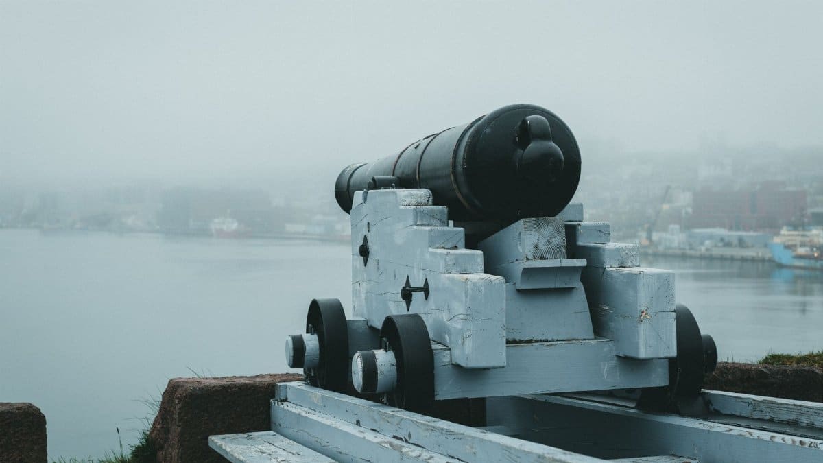 A historic cannon aimed at the misty seaside from a fortress, evoking a sense of defense and history.